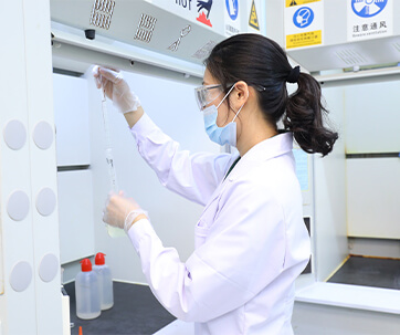women in lab coat looking at test tube wearing face mask with ponytail hair