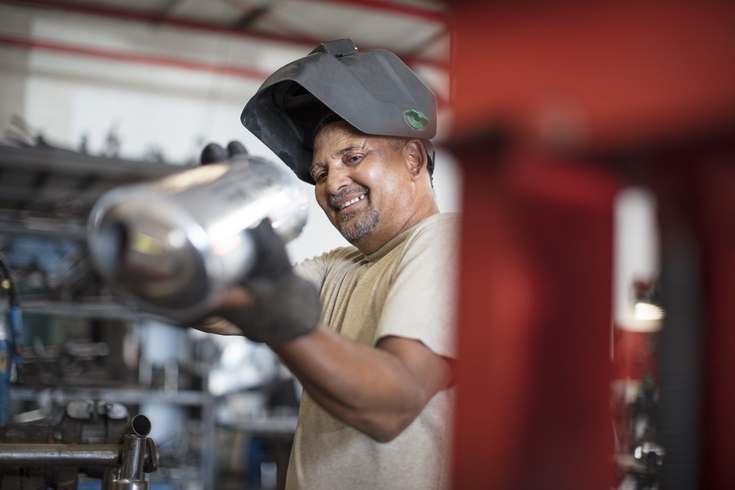 mechanic in workshop smiles as he inspects a catalytic converter